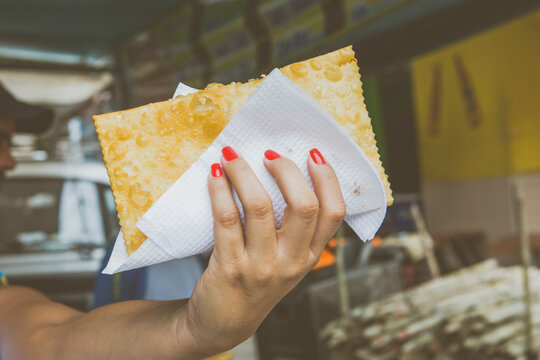 Pessoa segurando um pastel grande e frito em papel toalha durante festival de comida de rua em Belo Horizonte.