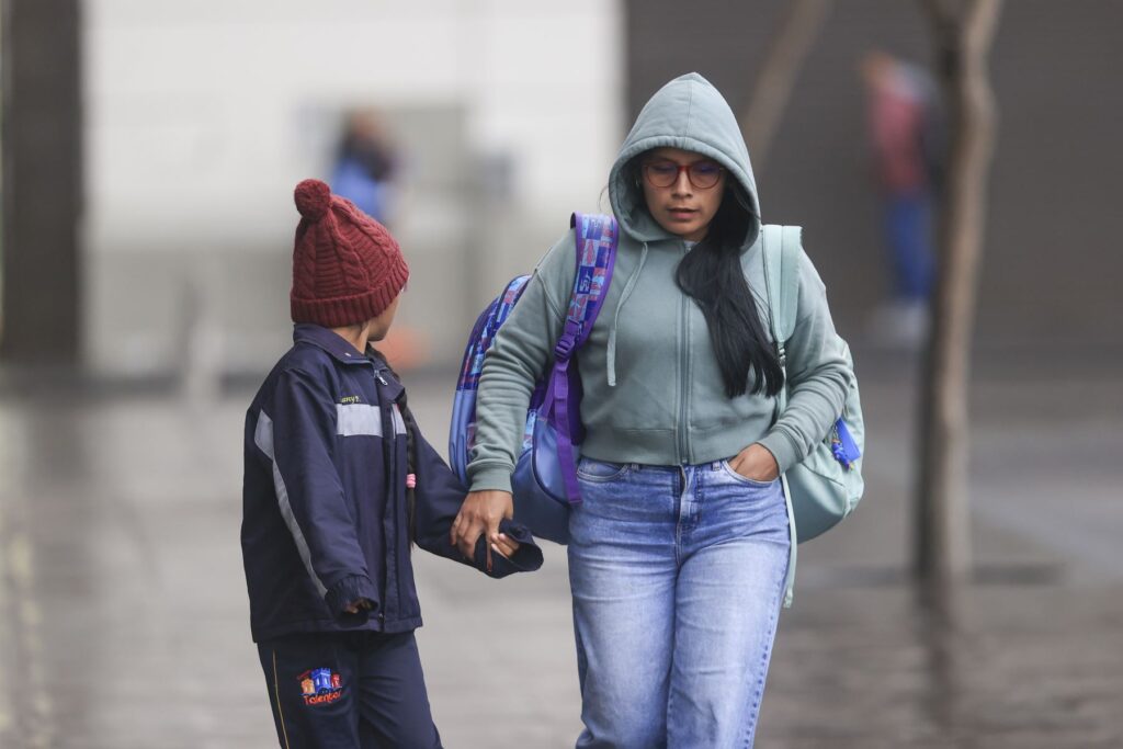 Mulher e criança vestindo roupas de frio caminham de mãos dadas pelas ruas de Belo Horizonte em uma manhã gelada.