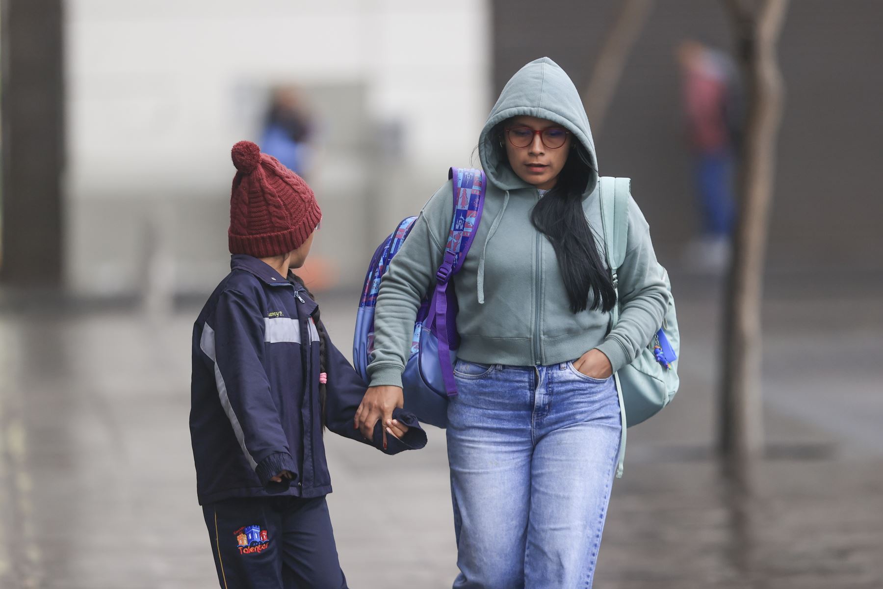 Mulher e criança vestindo roupas de frio caminham de mãos dadas pelas ruas de Belo Horizonte em uma manhã gelada.